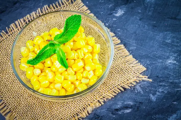 Canned corn in a glass plate on a gray concrete background.
