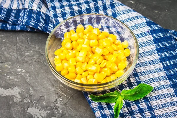 Canned corn in a glass plate on a gray concrete background. — Stock Photo, Image