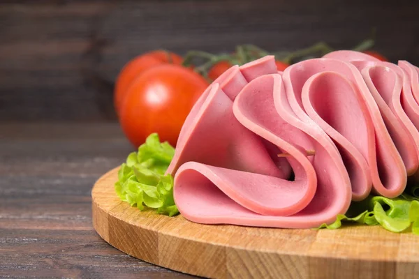 Salsicce affettate con foglie di insalata sullo sfondo di legno — Foto Stock