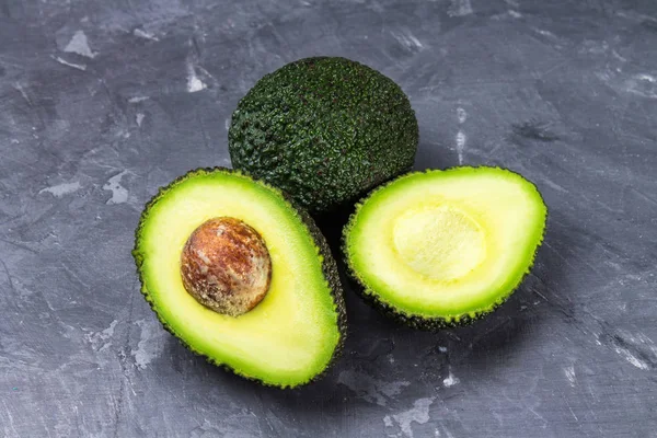 Geschnitten und ganze Avocado auf einem Holzbrett auf grauem Hintergrund. — Stockfoto