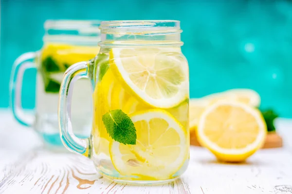 Banken mit Griffen mit kalter Limonade auf weißem Holzgrund. Zitronen. — Stockfoto