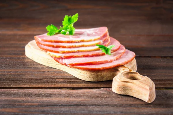 Taze yeşil salata ile dilimlenmiş jambon yuvarlak kesme tahtası üzerinde bırakır. Et ürünleri bir kahverengi ahşap tablo.
