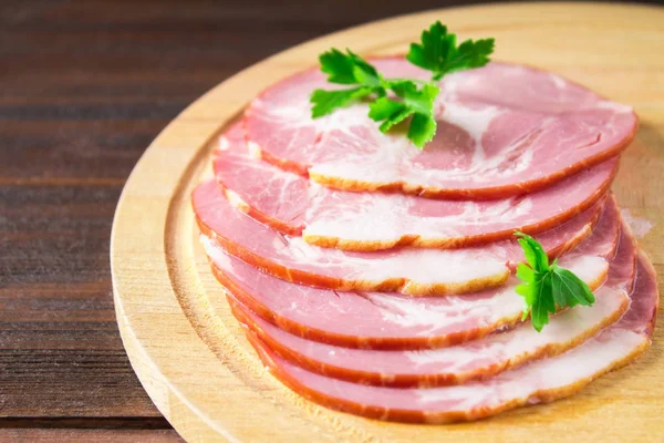 Taze yeşil salata ile dilimlenmiş jambon yuvarlak kesme tahtası üzerinde bırakır. Et ürünleri bir kahverengi ahşap tablo.