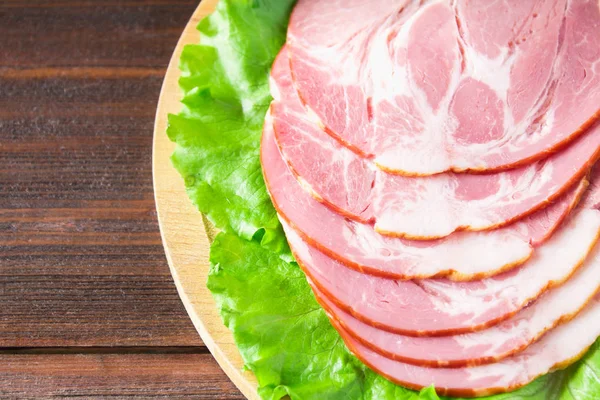 Taze yeşil salata ile dilimlenmiş jambon yuvarlak kesme tahtası üzerinde bırakır. Et ürünleri bir kahverengi ahşap tablo.