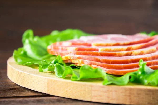 Taze yeşil salata ile dilimlenmiş jambon yuvarlak kesme tahtası üzerinde bırakır. Et ürünleri bir kahverengi ahşap tablo.