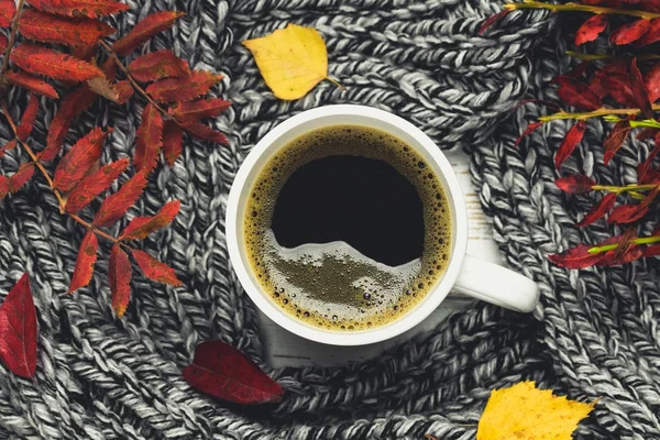 Örme bir eşarp ile ahşap bir masa üzerinde sonbahar ortamda sıcak kahve bir fincan kazak. Konfor, sıcaklık, rahat.