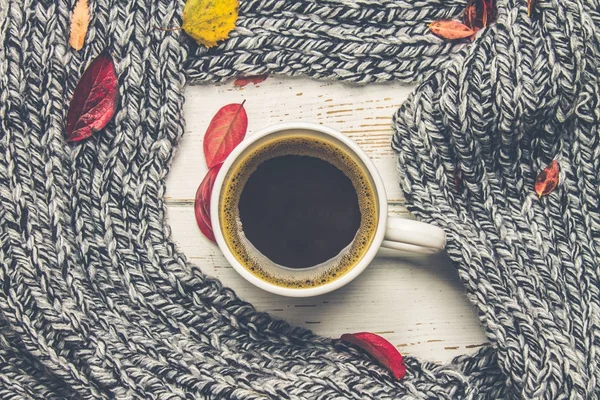 Örme bir eşarp ile ahşap bir masa üzerinde sonbahar ortamda sıcak kahve bir fincan kazak. Konfor, sıcaklık, rahat.