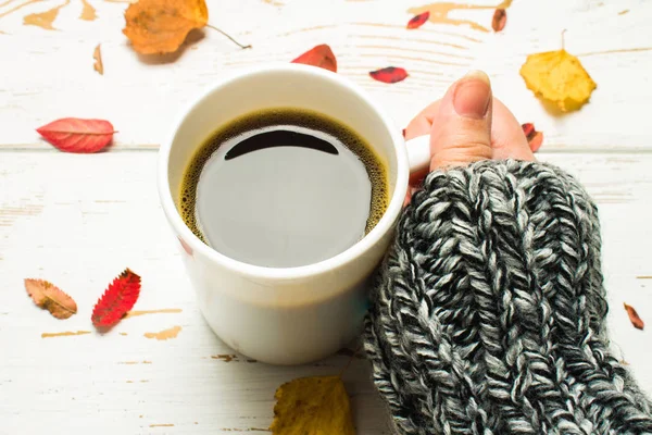 Bir kadının elinde bir kazak örme bir eşarp ile ahşap bir masa üzerinde sonbahar ortamda sıcak kahve bir fincan kazak. Konfor, sıcaklık, rahat.