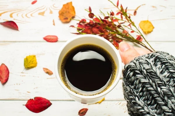 Горщик гарячої кави в руці жінки в светрі в осінній обстановці на дерев'яному столі з в'язаним шарфом, светром. Комфорт, тепло, затишок . — стокове фото