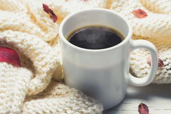 Örme bir eşarp ile ahşap bir masa üzerinde sonbahar ortamda sıcak kahve bir fincan kazak. Konfor, sıcaklık, rahat.