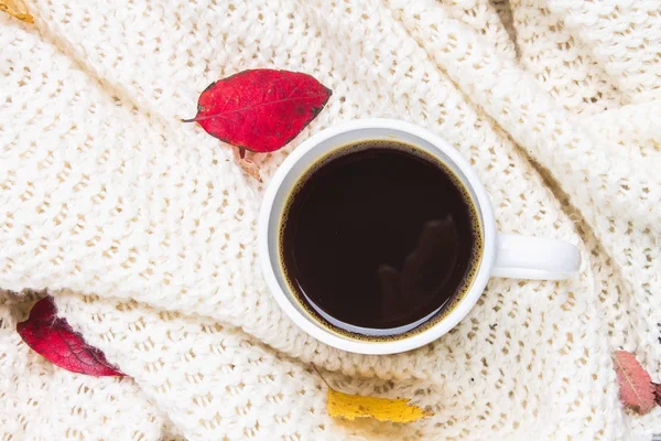 Örme bir eşarp ile ahşap bir masa üzerinde sonbahar ortamda sıcak kahve bir fincan kazak. Konfor, sıcaklık, rahat.