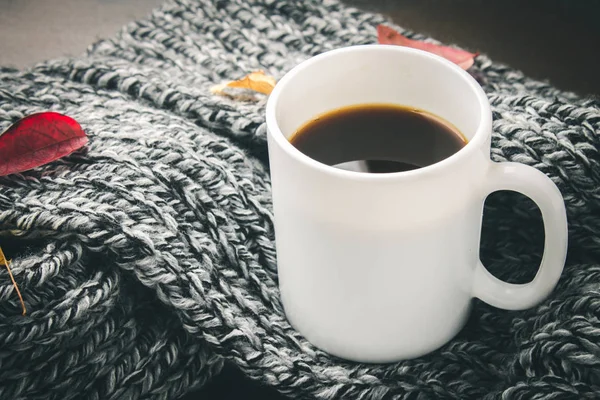 Örme bir eşarp ile ahşap bir masa üzerinde sonbahar ortamda sıcak kahve bir fincan kazak. Konfor, sıcaklık, rahat.