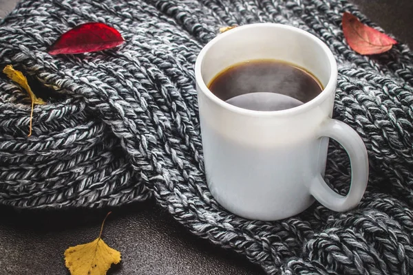 Örme bir eşarp ile ahşap bir masa üzerinde sonbahar ortamda sıcak kahve bir fincan kazak. Konfor, sıcaklık, rahat.