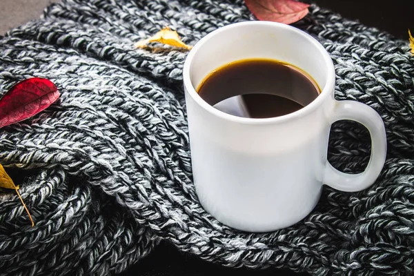 Örme bir eşarp ile ahşap bir masa üzerinde sonbahar ortamda sıcak kahve bir fincan kazak. Konfor, sıcaklık, rahat.