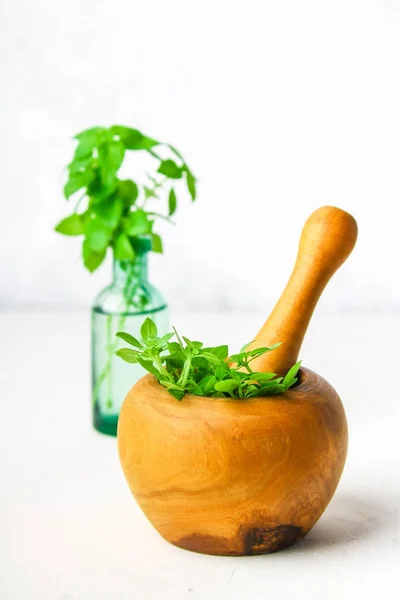 Albahaca verde limón en un mortero de madera sobre un fondo claro. Detrás de la albahaca en la botella . —  Fotos de Stock