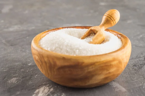 White sugar sugar in a wooden plate with a dustpan on a dark background.