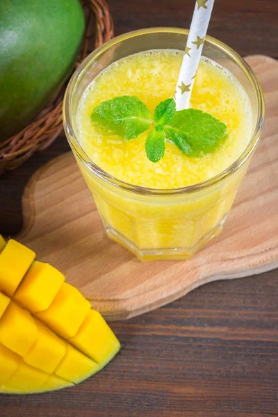 Saman ve nane bir cam ölçek ile smoothies mango. Dilimlenmiş mango ile plaka. Tropikal bir meyve. Ahşap arka plan
