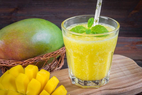 Saman ve nane bir cam ölçek ile smoothies mango. Dilimlenmiş mango ile plaka. Tropikal bir meyve. Ahşap arka plan