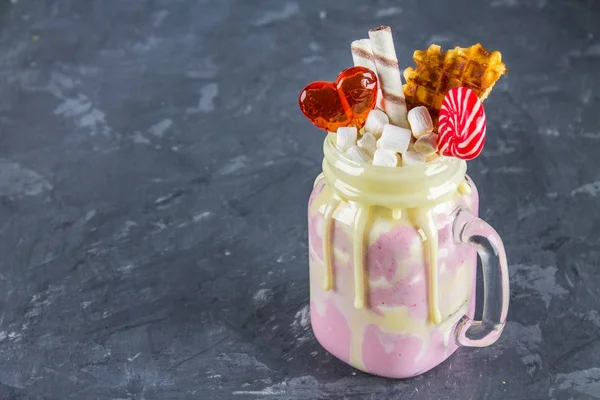 Pembe yüzlü, krem üzerinden Freakshake. Lolipop, waffle ve hatmi ile Monstershake. Bir Mason kavanoza aşırı milkshake. Koyu gri beton arka plan.
