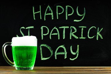 Bir kara tahta üzerinde yeşil tebeşir ile Yazıt: mutlu St. Patrick's günü. Yeşil bira ile bir kupa.