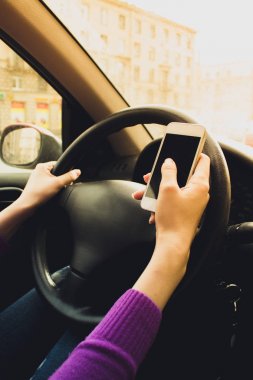 Kadın elinde telefon. Direksiyonun arkasında bir arabadaki kızla.