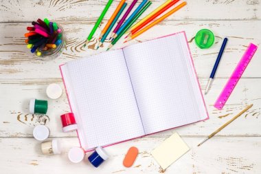 Yazıtlar için boş alanı beyaz bir ahşap zemin üzerine açık defter okul tarafından çevrili malzemeleri.