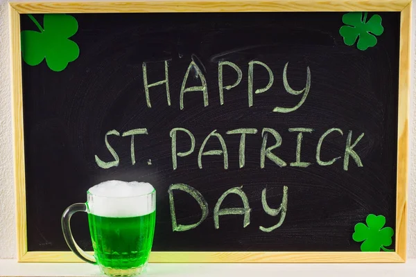 The inscription with green chalk on a chalkboard: Happy St. Patrick's Day. Clover leaves. A mug with green beer. — Stock Photo, Image