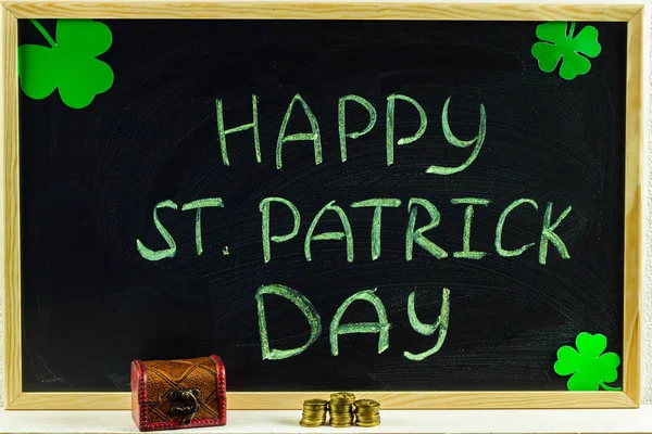 La inscripción con tiza verde en una pizarra: Feliz Día de San Patricio. Hojas de trébol. Pecho con monedas . — Foto de Stock