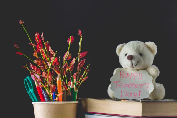 Concept of Teacher's Day. Objects on a chalkboard background. Books, green apple, bear with a sign: Happy Teacher's Day, pencils and pens in a glass, twig with autumn leaves. — Stock Photo, Image