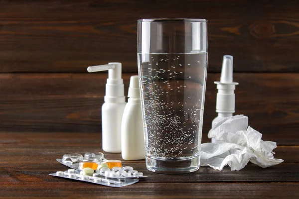 Um copo de água, um spray para o nariz, gotas nasais, comprimidos na bolha, doces da tosse na mesa. Medicamentos modernos para constipações, gripe. Tratamento da doença . — Fotografia de Stock