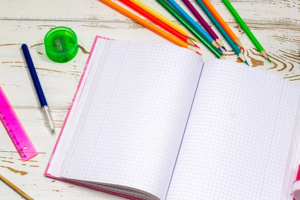 Caderno ao ar livre cercado por material escolar em um fundo de madeira branco com espaço vazio para inscrições . — Fotografia de Stock