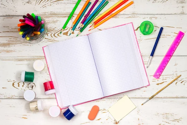 Caderno ao ar livre cercado por material escolar em um fundo de madeira branco com espaço vazio para inscrições . — Fotografia de Stock