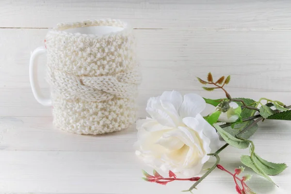 Кружка в вязаном свитере, белая роза на столе — стоковое фото
