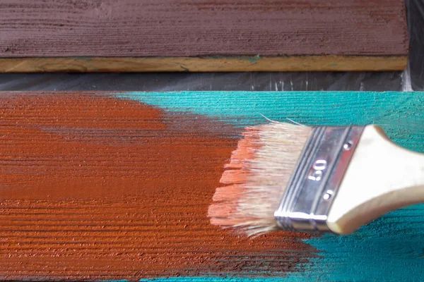 Brush with paint in hand. A man paints blue boards in a brown paint brush.