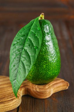 Bir kesme tahtası ahşap bir kahverengi masa üzerinde bir yeşil ham olgunlaşmış bütün avokado meyve yaprakla açıktır.