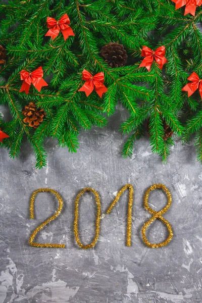 Spar takken met kegels en red strikken bovenop een grijze concrete achtergrond. Kerst Nieuwjaar. Tekst 2018 van goud tinsel. — Stockfoto