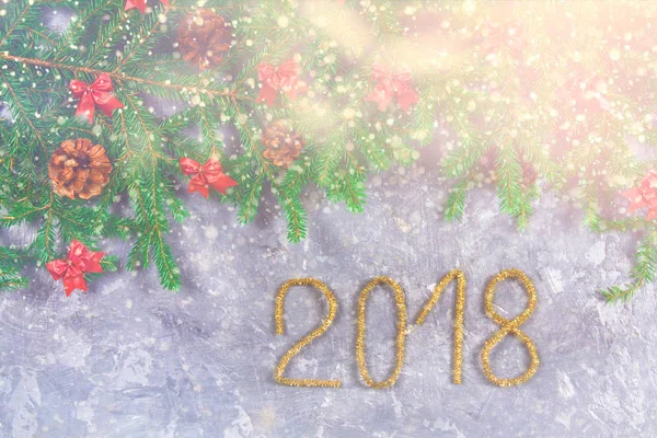 Spar takken met kegels en red strikken bovenop een grijze concrete achtergrond. Kerst Nieuwjaar. Tekst 2018 van goud tinsel. — Stockfoto