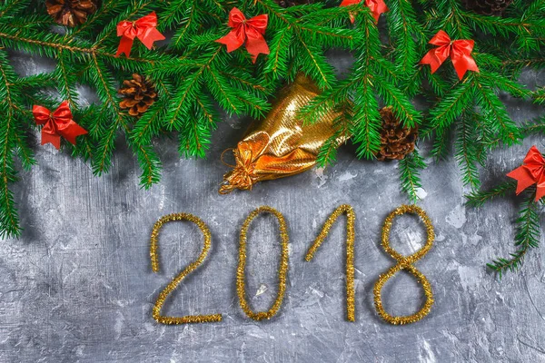 Ramas de abeto con conos y arcos rojos sobre un fondo de hormigón gris. Año Nuevo Navidad. Texto 2018 de oropel dorado . — Foto de Stock