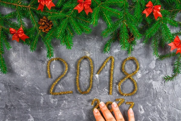 Spar takken met kegels en red strikken bovenop een grijze concrete achtergrond. Kerst Nieuwjaar. Tekst 2018 van goud tinsel. — Stockfoto
