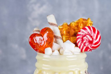 Pembe yüzlü, krem üzerinden Freakshake. Lolipop, waffle ve hatmi ile Monstershake. Bir Mason kavanoza aşırı milkshake. Koyu gri beton arka plan.