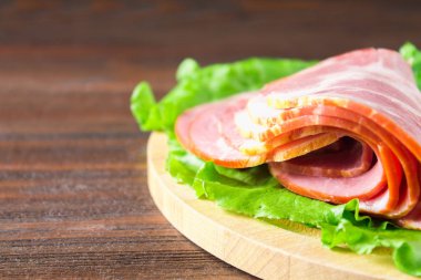 Taze yeşil salata ile dilimlenmiş jambon yuvarlak kesme tahtası üzerinde bırakır. Et ürünleri bir kahverengi ahşap tablo.
