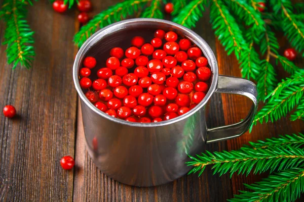 Morse ou chá de cowberry em uma caneca de lata, cercada por ramos de abeto em uma mesa de madeira . — Fotografia de Stock