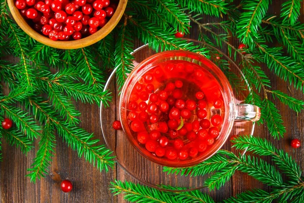 Chá quente de cranberries em uma xícara de vidro cercada por ramos de abeto em uma mesa de madeira . — Fotografia de Stock