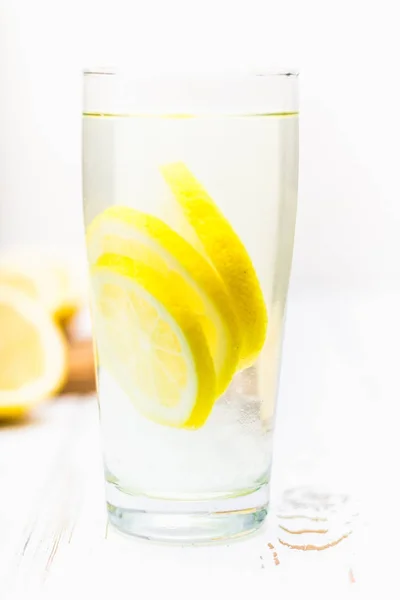 Скляний стакан і глечик холодного лимонаду на білому дерев'яному фоні в оточенні лимонів . — стокове фото