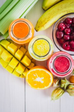 Mango, portakal, muz, kereviz, çilek, ahşap bir masa üzerinde şişelerde çok renkli smoothies.