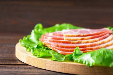 Taze yeşil salata ile dilimlenmiş jambon yuvarlak kesme tahtası üzerinde bırakır. Et ürünleri bir kahverengi ahşap tablo.