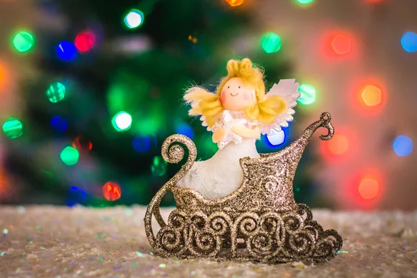 Рождественский ангел в санях на фоне рождественской елки, гирлянды, боке . — стоковое фото