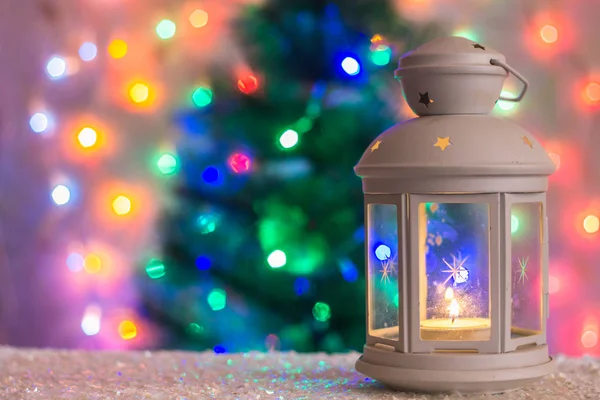 Vánoční bílá Lucerna s hořící svíčkou na pozadí stromeček, světla girlandy, bokeh. — Stock fotografie