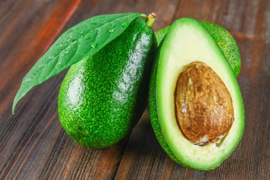 Üç yeşil ham olgunlaşmış avokado meyve ve yaprakları kahverengi ahşap bir masa üzerinde bir kemiği ile kesilmiş bir buçuk.