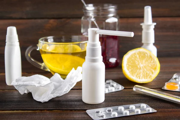 Saúde, medicina tradicional e conceito de gripe - xícara de chá com limão, termômetro e drogas na mesa de madeira . — Fotografia de Stock